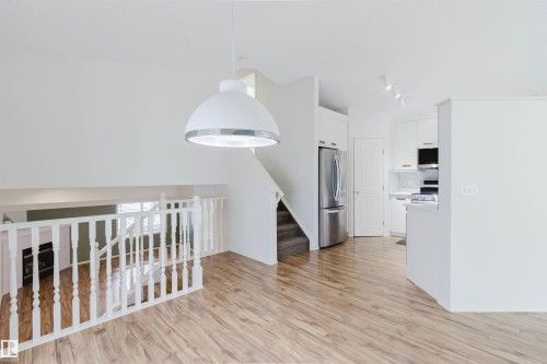 Open concept interior featuring wood-finish flooring and a white spindle railing - 1694 Tompkins Wynd Nw, Edmonton, AB - Indoor