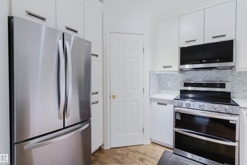 Kitchen featuring stainless steel appliances, white cabinetry with silver hardware, light-colored countertops, a subway tile backsplash, and wood-finish flooring - 1694 Tompkins Wynd Nw, Edmonton, AB - Indoor Photo Showing Kitchen With Stainless Steel Kitchen