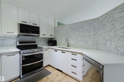 Kitchen featuring white cabinetry, stainless steel appliances, quartz countertops, a tile backsplash, and wood-finish flooring - 1694 Tompkins Wynd Nw, Edmonton, AB - Indoor Photo Showing Kitchen With Double Sink