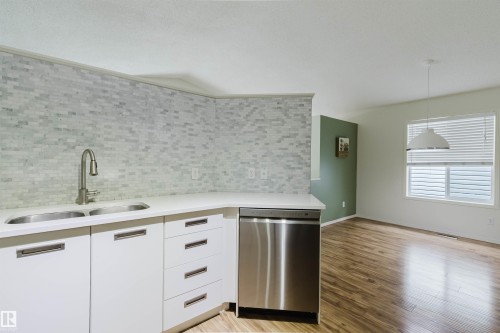 Kitchen area featuring white cabinetry, a stainless steel double sink with a gooseneck faucet, a white countertop, and a light-toned mosaic tile backsplash - 1694 Tompkins Wynd Nw, Edmonton, AB - Indoor Photo Showing Kitchen With Double Sink