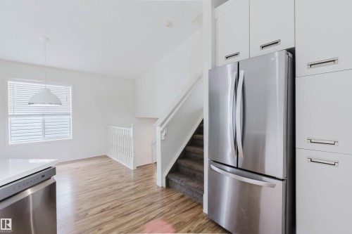 Contemporary kitchen featuring a stainless steel French door refrigerator, white cabinetry with integrated hardware, and a white countertop - 1694 Tompkins Wynd Nw, Edmonton, AB - Indoor