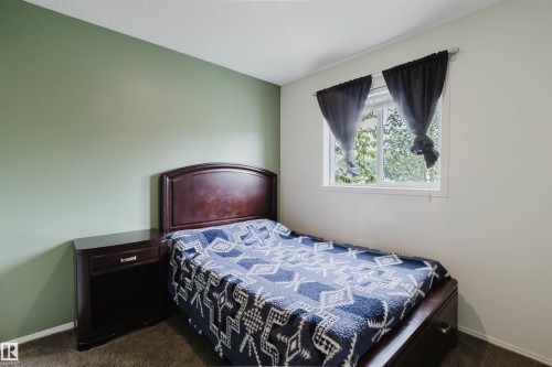 Bedroom featuring a window with exterior tree scenery, two-tone painted walls, and dark wood-finish built-in shelving - 1694 Tompkins Wynd Nw, Edmonton, AB - Indoor Photo Showing Bedroom