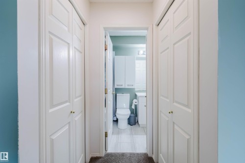 Hallway featuring bi-fold panel doors with brass hardware, leading to a bathroom with a toilet, vanity, and overhead cabinetry - 1694 Tompkins Wynd Nw, Edmonton, AB - Indoor