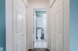 Hallway featuring bi-fold panel doors with brass hardware, leading to a bathroom with a toilet, vanity, and overhead cabinetry - 