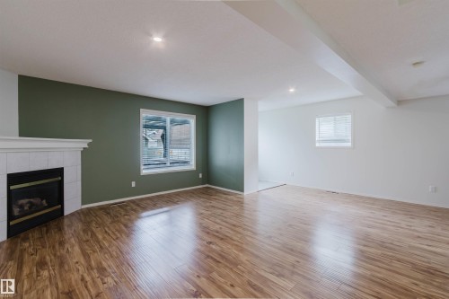 Spacious room featuring wood-finish flooring, a corner fireplace with a white tile surround and mantel, and recessed lighting - 1694 Tompkins Wynd Nw, Edmonton, AB - Indoor With Fireplace