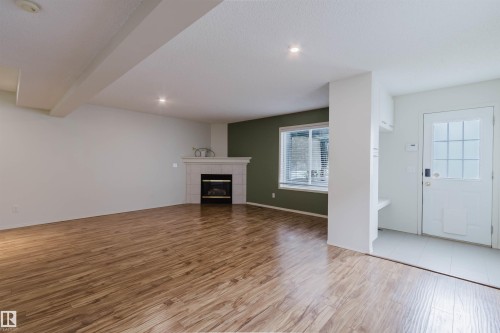 Spacious living area featuring wood-finish flooring, a tiled fireplace with a white mantel, and recessed lighting - 1694 Tompkins Wynd Nw, Edmonton, AB - Indoor With Fireplace