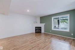 Spacious interior with wood-finish flooring, a corner fireplace featuring a white mantel, and a window with blinds - 