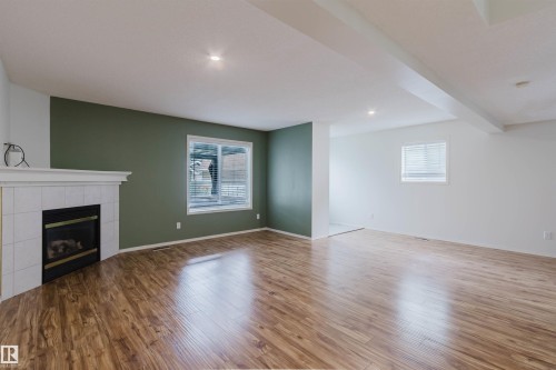 Living area featuring a corner fireplace with a white tile surround and mantel - 1694 Tompkins Wynd Nw, Edmonton, AB - Indoor With Fireplace