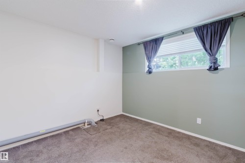 Carpeted interior space featuring a window with integrated blinds, a light green accent wall, and white trim - 1694 Tompkins Wynd Nw, Edmonton, AB - Indoor Photo Showing Other Room