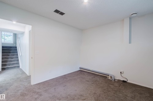 Carpeted room featuring white walls, recessed lighting, and a visible staircase with a window - 1694 Tompkins Wynd Nw, Edmonton, AB - Indoor Photo Showing Other Room