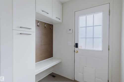 Entryway featuring a white paneled door with frosted window inserts, a built-in bench, and integrated white cabinetry - 1694 Tompkins Wynd Nw, Edmonton, AB - Indoor Photo Showing Other Room