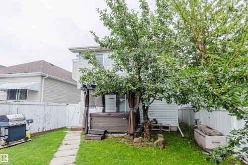 Expansive backyard featuring a hot tub with privacy curtains, mature trees, a manicured lawn, and concrete paver pathway - 1694 Tompkins Wynd Nw, Edmonton, AB - Outdoor