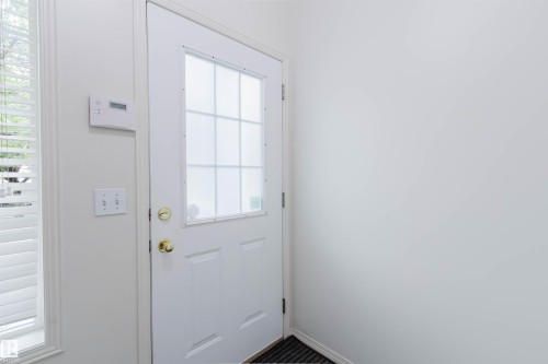 White paneled entry door with an upper window featuring grid inserts and brass hardware - 1694 Tompkins Wynd Nw, Edmonton, AB - Indoor Photo Showing Other Room
