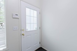White paneled entry door with an upper window featuring grid inserts and brass hardware - 