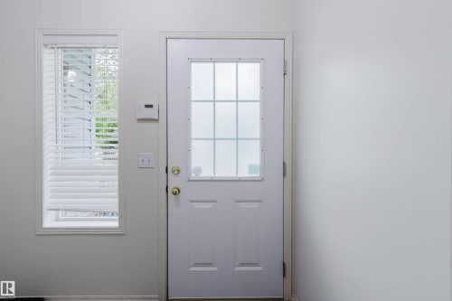 Entry door with a multi-pane frosted glass insert and brass hardware, complemented by an adjacent window with white blinds - 1694 Tompkins Wynd Nw, Edmonton, AB - Indoor Photo Showing Other Room