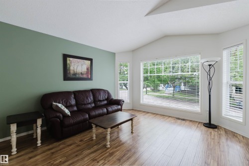 Spacious living area featuring wood-finish flooring, a vaulted ceiling, and multiple large windows with white blinds - 1694 Tompkins Wynd Nw, Edmonton, AB - Indoor Photo Showing Living Room