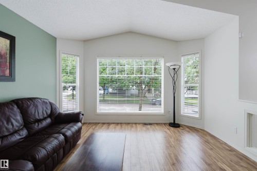 Vaulted ceiling living area featuring multiple windows with blinds, wood-finish flooring, and a neutral color palette - 1694 Tompkins Wynd Nw, Edmonton, AB - Indoor Photo Showing Living Room With Fireplace