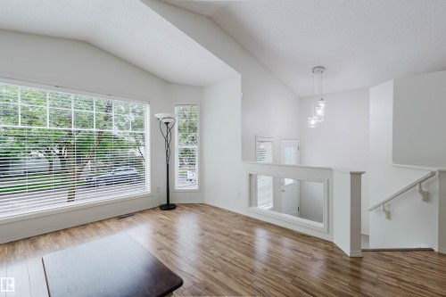 Vaulted ceiling living space featuring a large picture window, wood-finish flooring, a built-in railing, and a contemporary pendant light fixture - 1694 Tompkins Wynd Nw, Edmonton, AB - Indoor Photo Showing Other Room