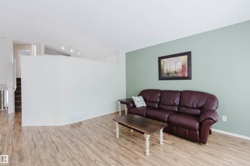 Spacious living area featuring wood-finish flooring, light green accent wall, and a staircase with white balusters - 1694 Tompkins Wynd Nw, Edmonton, AB - Indoor Photo Showing Living Room