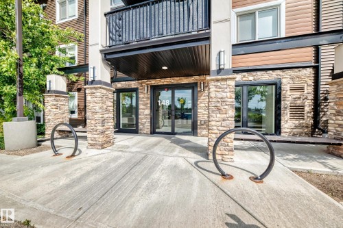 Building entrance with stone facade, dark siding, and large glass doors - #322 148 Ebbers Bv Nw, Edmonton, AB - Outdoor With Balcony