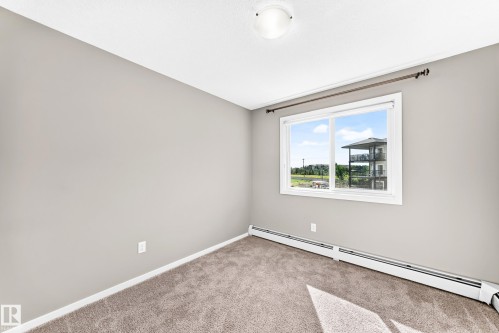 Neutral wall color, carpeted flooring, large window, baseboard heating, ceiling-mounted light fixture - #322 148 Ebbers Bv Nw, Edmonton, AB - Indoor Photo Showing Other Room