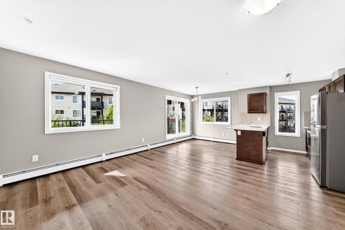 Wood-finish flooring, light gray wall paint, white trim, sliding glass door, and a kitchen island with a light-toned countertop - #322 148 Ebbers Bv Nw, Edmonton, AB - Indoor