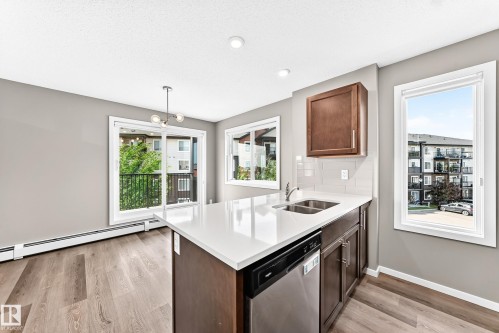 Wood-finish flooring, white countertops, built-in stainless steel dishwasher, and sliding glass door to a balcony - #322 148 Ebbers Bv Nw, Edmonton, AB - Indoor Photo Showing Kitchen With Double Sink