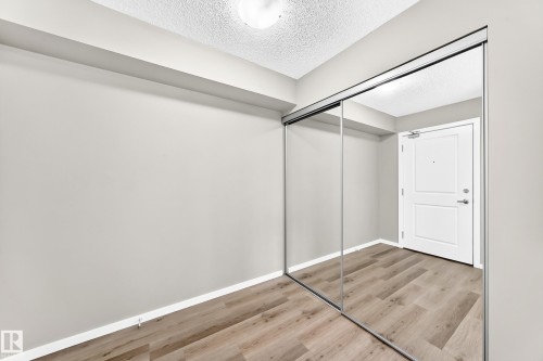 Wood-finish flooring with a neutral wall color, mirrored sliding closet doors, and recessed lighting - #322 148 Ebbers Bv Nw, Edmonton, AB - Indoor Photo Showing Other Room