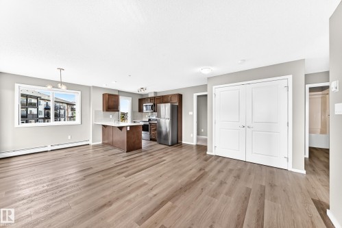 Open-concept living space featuring wood-finish flooring, a kitchen with stainless steel appliances, dark wood cabinetry, and a breakfast bar - #322 148 Ebbers Bv Nw, Edmonton, AB - Indoor