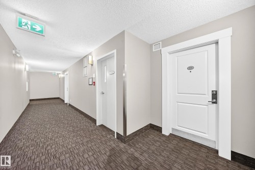 Textured carpet flooring, neutral painted walls, white trim, and wall-mounted light fixtures - #322 148 Ebbers Bv Nw, Edmonton, AB - Indoor Photo Showing Other Room