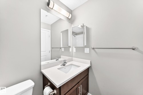 Vanity with white countertop, chrome faucet, and wood-finish cabinetry - #322 148 Ebbers Bv Nw, Edmonton, AB - Indoor Photo Showing Bathroom