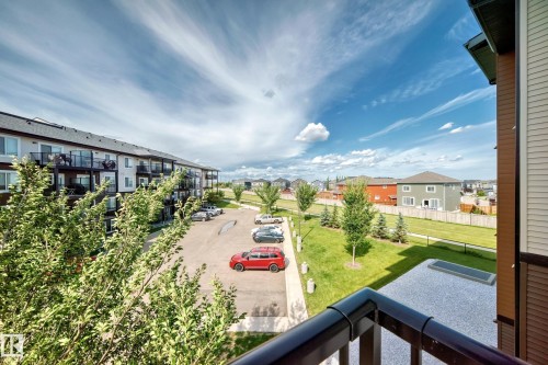 Apartment building exterior with multiple balconies, a paved parking area, and a landscaped green space with mature trees - #322 148 Ebbers Bv Nw, Edmonton, AB - Outdoor