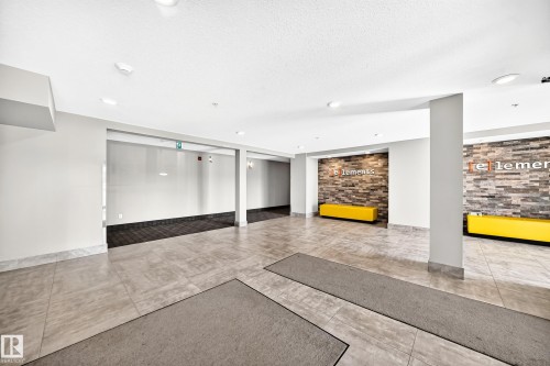 Spacious common area featuring large format tile flooring, recessed lighting, and an accent wall with stacked stone detailing - #322 148 Ebbers Bv Nw, Edmonton, AB - Indoor Photo Showing Other Room