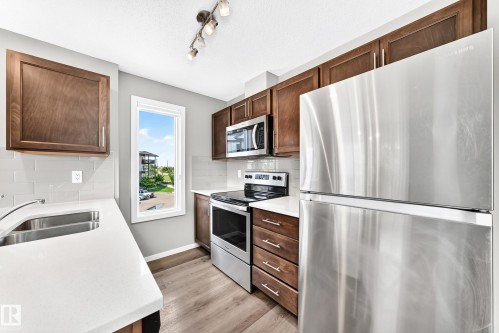Kitchen featuring stainless steel appliances, wood-finish cabinetry, white countertops, subway tile backsplash, and wood-finish flooring - #322 148 Ebbers Bv Nw, Edmonton, AB - Indoor Photo Showing Kitchen With Double Sink