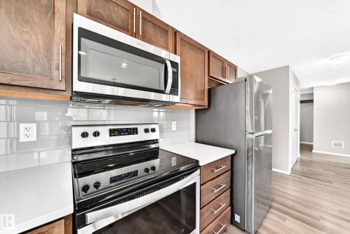Kitchen featuring wood-finish cabinetry, stainless steel appliances, white countertops, and a subway tile backsplash - #322 148 Ebbers Bv Nw, Edmonton, AB - Indoor Photo Showing Kitchen