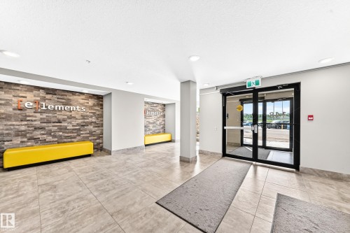 Tiled flooring throughout, accent walls featuring stacked stone, recessed lighting, and automatic glass entry doors - #322 148 Ebbers Bv Nw, Edmonton, AB - Indoor Photo Showing Other Room
