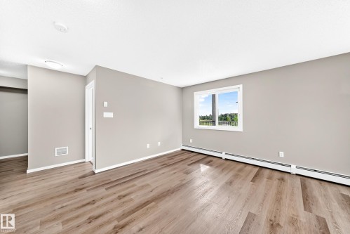 Wood-finish flooring, neutral wall tones, white trim, and a window with a green landscape backdrop - #322 148 Ebbers Bv Nw, Edmonton, AB - Indoor Photo Showing Other Room