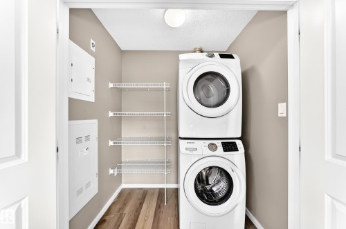 Laundry closet featuring a stacked washer and dryer, wire shelving, and wood-finish flooring - #322 148 Ebbers Bv Nw, Edmonton, AB - Indoor Photo Showing Laundry Room