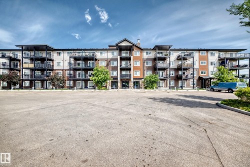 Multi-story building featuring private balconies, individual patios on the ground level, and a large paved parking area - #322 148 Ebbers Bv Nw, Edmonton, AB - Outdoor With Balcony With Facade