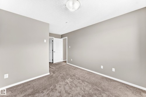 Neutral-toned walls, textured carpeting, white trim, and a flush-mount ceiling light fixture - #322 148 Ebbers Bv Nw, Edmonton, AB - Indoor Photo Showing Other Room