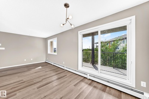 Open-concept room featuring wood-finish flooring, a contemporary chandelier, a large sliding glass door, an exterior balcony with a black railing, and a secondary window - #322 148 Ebbers Bv Nw, Edmonton, AB - Indoor Photo Showing Other Room