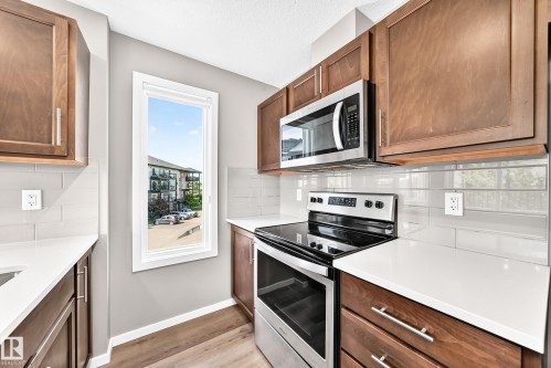 Kitchen featuring wood cabinetry, light countertops, subway tile backsplash, stainless steel appliances, and wood-finish flooring - #322 148 Ebbers Bv Nw, Edmonton, AB - Indoor Photo Showing Kitchen With Upgraded Kitchen