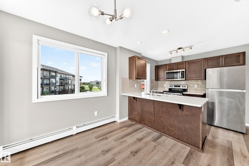 Kitchen featuring stainless steel appliances, dark wood-finish cabinetry, and light countertops - #322 148 Ebbers Bv Nw, Edmonton, AB - Indoor Photo Showing Kitchen