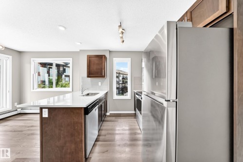Kitchen featuring a central island with a sink, stainless steel appliances, wood-finish cabinetry, and wood-finish flooring - #322 148 Ebbers Bv Nw, Edmonton, AB - Indoor Photo Showing Kitchen