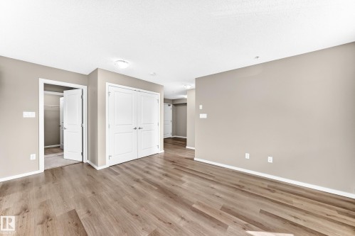 Wood-finish flooring, neutral wall tones, white trim, recessed lighting, and white paneled doors - #322 148 Ebbers Bv Nw, Edmonton, AB - Indoor Photo Showing Other Room