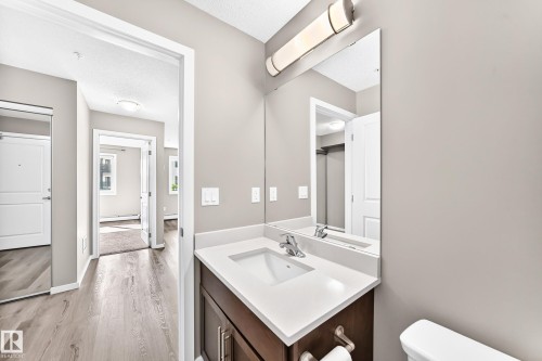 Bathroom vanity featuring a single basin sink, white countertop, and dark wood-finish cabinetry - #322 148 Ebbers Bv Nw, Edmonton, AB - Indoor Photo Showing Bathroom