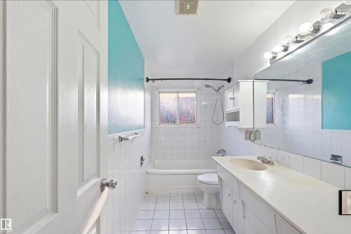 Bathroom featuring a built-in vanity with a single basin sink, extensive wall tiling, and an integrated bathtub with shower - 13604 90A Street Nw, Edmonton, AB - Indoor Photo Showing Bathroom