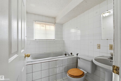 White ceramic tile walls with a decorative border, pedestal sink, and built-in bathtub with tile surround - 13604 90A Street Nw, Edmonton, AB - Indoor Photo Showing Bathroom