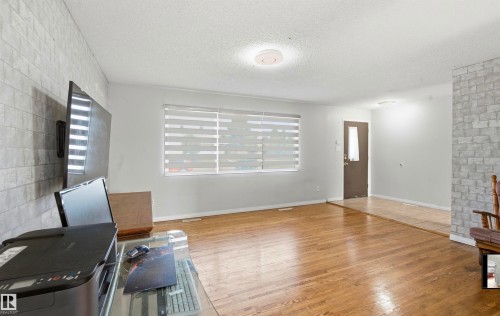 Hardwood flooring, textured accent wall, window with horizontal blinds, and a solid entry door with frosted glass insert - 13604 90A Street Nw, Edmonton, AB - Indoor With Fireplace