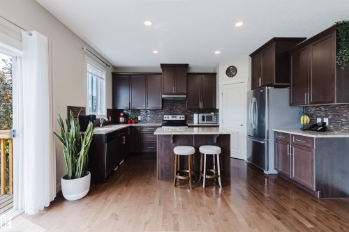 Open-concept kitchen featuring wood-finish flooring, dark wood cabinetry, stainless steel appliances, and recessed lighting - 3843 Agar Green Sw, Edmonton, AB - Indoor Photo Showing Kitchen With Stainless Steel Kitchen With Upgraded Kitchen